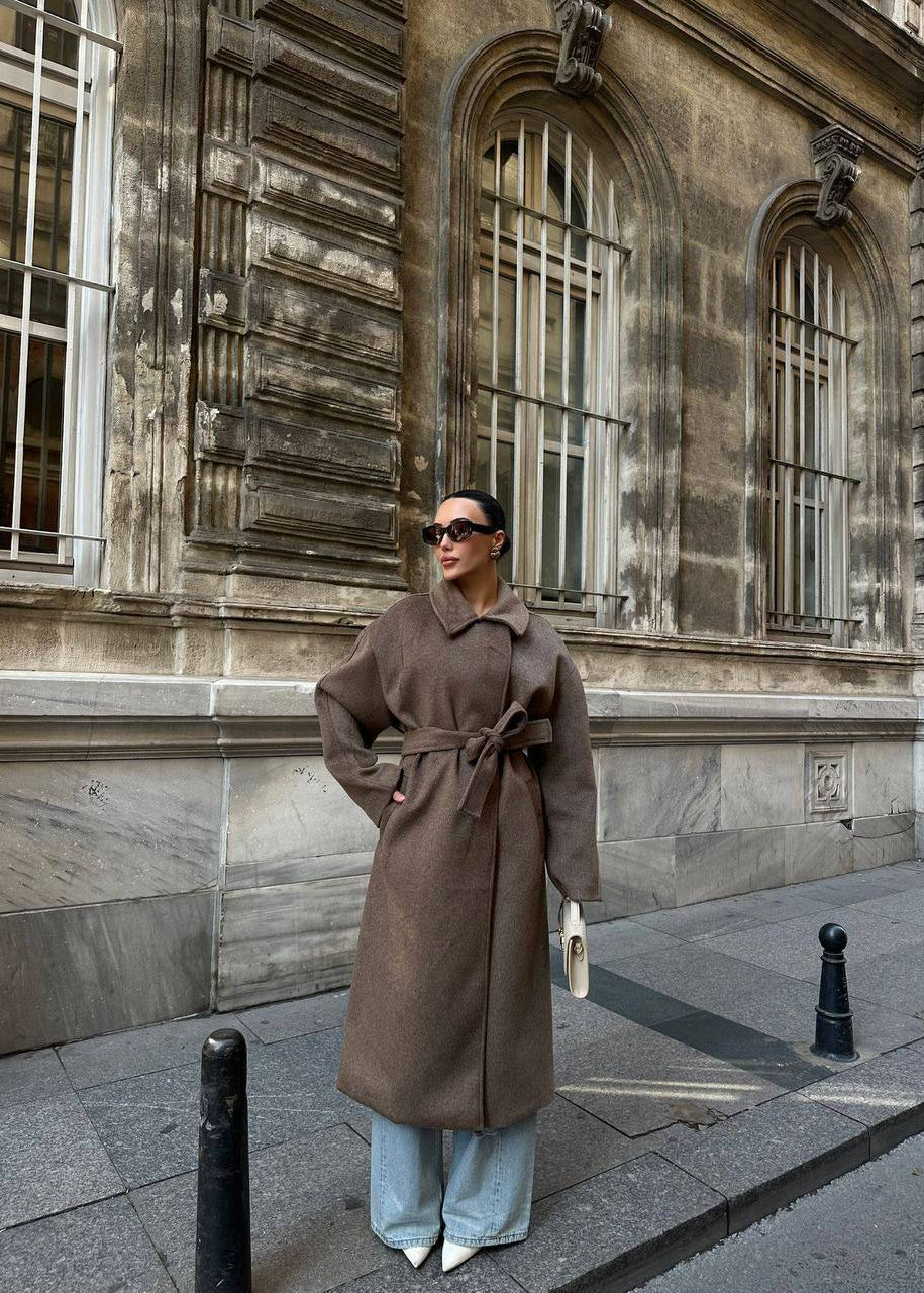 Manteau long femme, manteau oversize, manteau ceinturé, pardessus femme, manteau d'hiver, manteau mi-saison.
Style : Chic, élégant, décontracté, moderne, tendance, sophistiqué, minimaliste, urbain, intemporel, cocooning.
Couleur : Marron clair, taupe, grège, camel clair, uni.
Caractéristiques : Coupe oversize, col à revers classique, ceinture à nouer, manches longues, tissu doux, doublé (si c'est le cas), poches latérales (si visibles), longueur midi/longue.
Matière (supposée) : Drap de laine, laine mélang