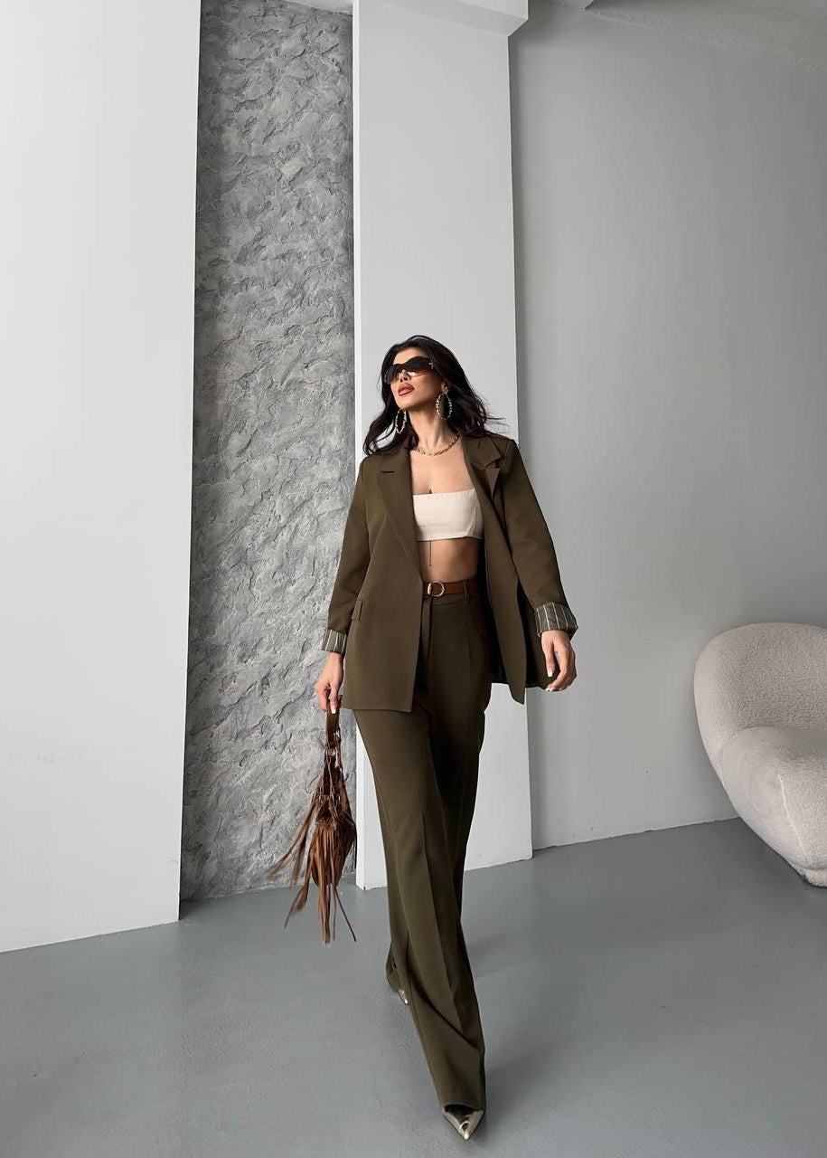 Affirmez votre style avec notre ensemble tailleur qui marie coupe décontractée et sophistication urbaine. Dans une teinte vert kaki (ou olive) profonde, cet ensemble est la pièce maîtresse d'un look moderne et affirmé.

La veste arbore une coupe oversize et droite pour une allure désinvolte, structurée par un revers classique. Le détail des manches retroussées avec doublure rayée apporte une touche d'originalité et de légèreté.

Le pantalon, à la coupe fluide et droite, épouse la tendance actuelle, garantis
